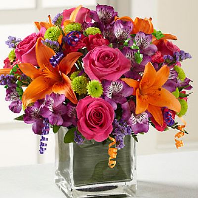 Birthday blooms that are ready to get your recipient's special day started, this flower bouquet is bright, happy, and ready to celebrate! Hot pink roses and orange Asiatic Lilies are vibrant and fun surrounded by purple Peruvian Lilies, hot pink mini carnations, green button poms, purple statice, and an assortment of lush greens. Accented with assorted curling ribbons to give it that party feels and presented in a clear glass cubed vase lined with ti leaf green material for added beauty, this unforgettable birthday bouquet is that ultimate surprise that will make them feel the love on their big day.

STANDARD bouquet includes 11 stems.
Approximately 10H x 10W.
C Quantity Color Description
2 Hot Pink 50 cm Standard Rose
1 Orange Asiatic Lily
3 Purple Alstroemeria
2 Green Button Pom
2 Hot Pink Miniature Carnation
1 Purple Filler - Sinuata Statice
2 Green Green - Leather Leaf
1 Green Green - Pittosporum
0.33 Green Green Flexible Leaf Material
1.5 Curling Ribbon (yds.)
0.33 Green Florist Foam Brick

DELUXE bouquet includes 15 stems.
Approximately 11H x 11W.
C Quantity Color Description
4 Hot Pink 50 cm Standard Rose
1 Orange Asiatic Lily
3 Purple Alstroemeria
2 Green Button Pom
3 Hot Pink Miniature Carnation
2 Purple Filler - Sinuata Statice
2 Green Green - Leather Leaf
1 Green Green - Pittosporum
0.33 Green Green Flexible Leaf Material
1.5 Curling Ribbon (yds.)
0.33 Green Florist Foam Brick

PREMIUM bouquet includes 19 stems.
Approximately 12H x 12W.
C Quantity Color Description
5 Hot Pink 50 cm Standard Rose
2 Orange Asiatic Lily
4 Purple Alstroemeria
3 Green Button Pom
3 Hot Pink Miniature Carnation
2 Purple Filler - Sinuata Statice
2 Green Green - Leather Leaf
1 Green Green - Pittosporum
0.66 Green Green Flexible Leaf Material
3 Curling Ribbon (yds.)
0.5 Green Florist Foam Brick