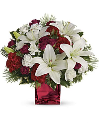 <p>Filled with holiday charm. Red spray roses and white asiatic lilies are arranged to perfection in our red mirrored cube.</p>